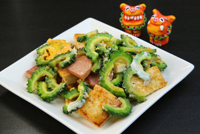 Goya Champuru with two shisa lion statues next to the plate