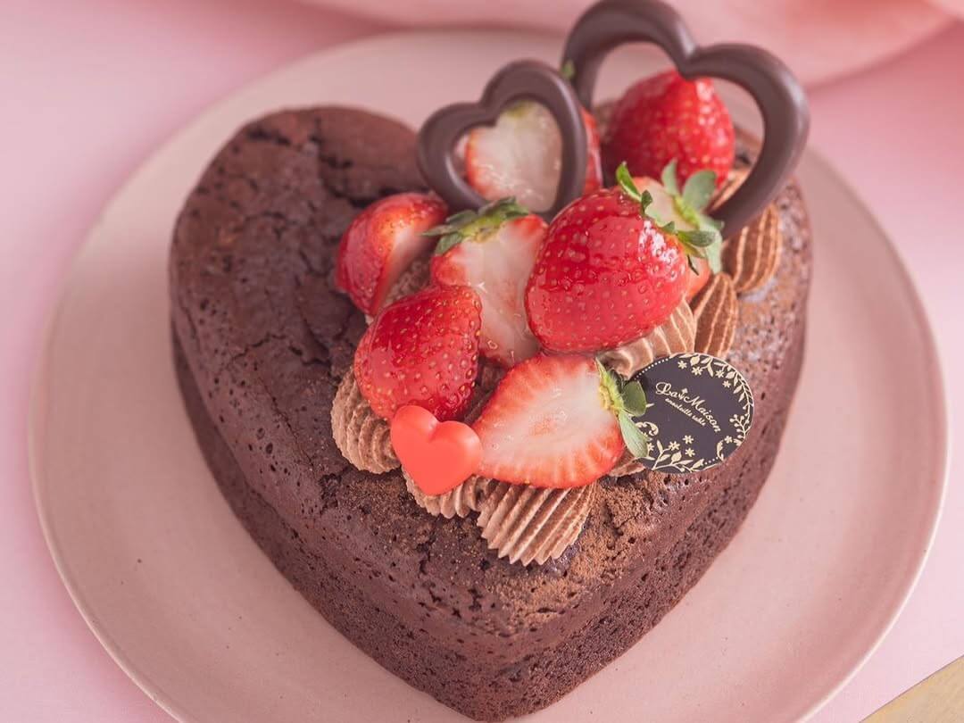 A heart shaped chocoalte cake with frosting, strawberries and chocolate on top