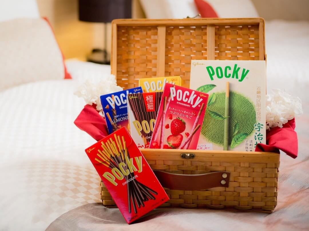 A wicker case on a hotel bed holds several boxes and flavors of Pocky