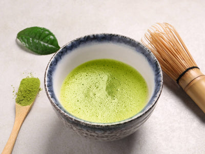A bowl of matcha green tea with a bamboo whisk and scooper